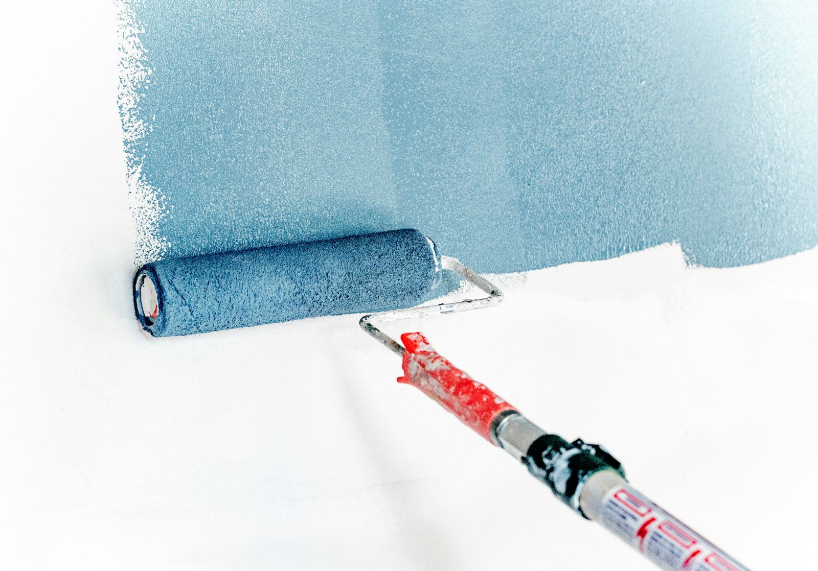 Close-up of a roller laying down a smooth, even coat of soft blue paint on a wall