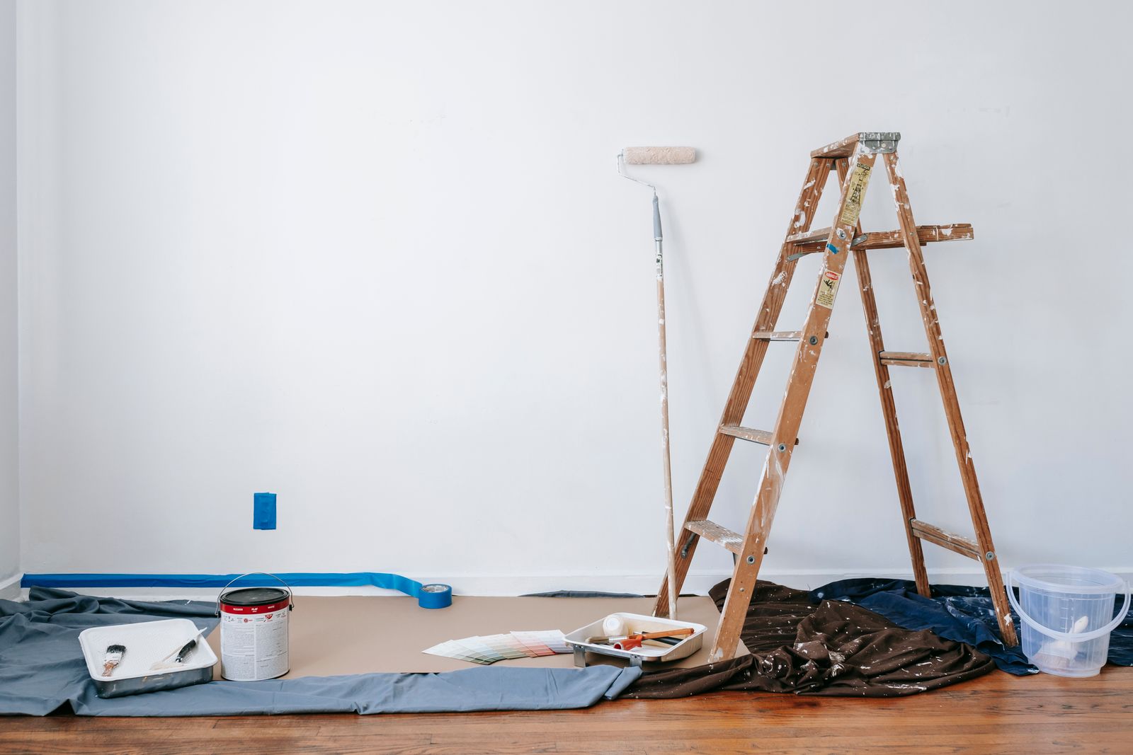 Interior painting prep — ladder, roller, paint cans, color swatches and drop cloths laid out in a room